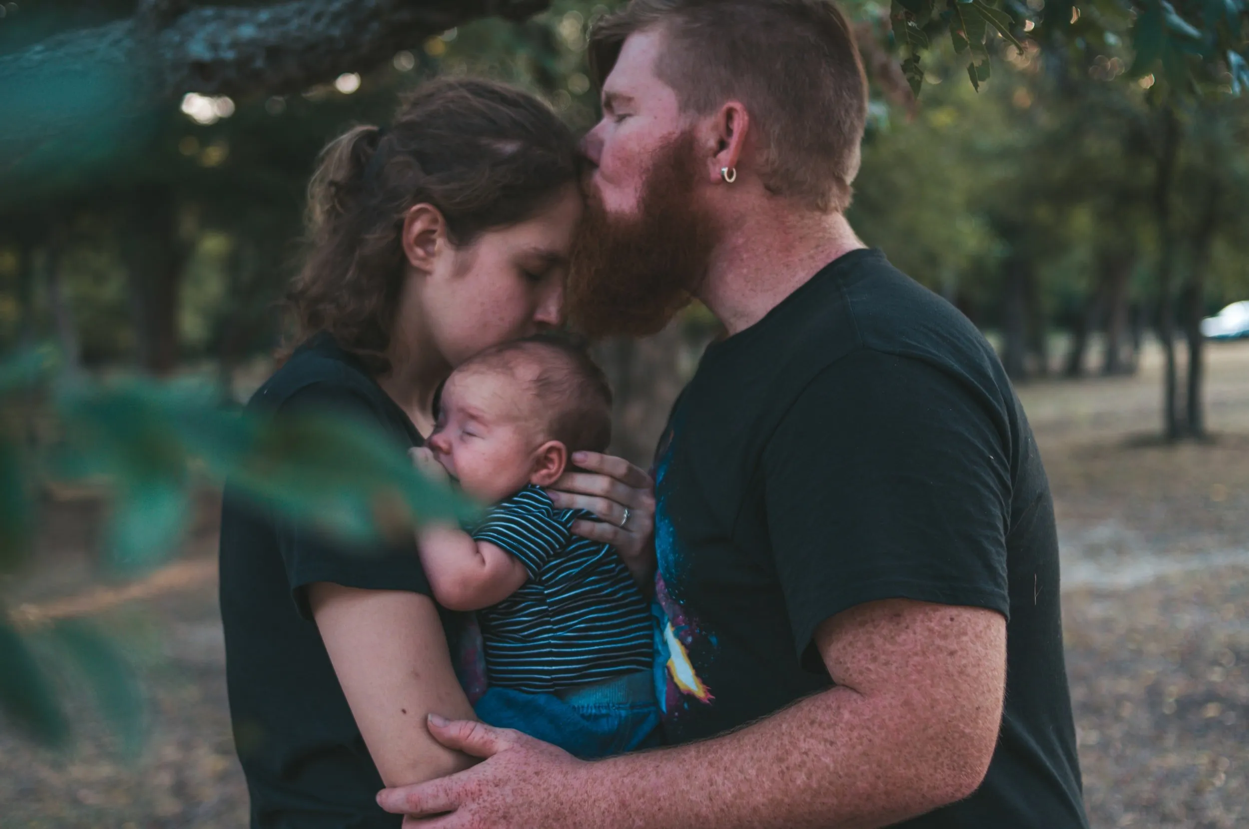 A couple embracing outdoors at dusk, holding their baby between them