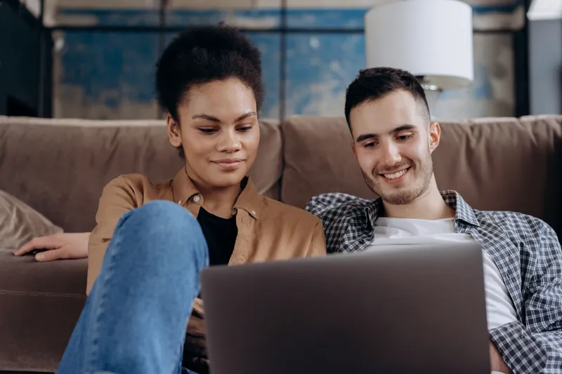 A couple at home on their couch, meeting with their counselor over a laptop