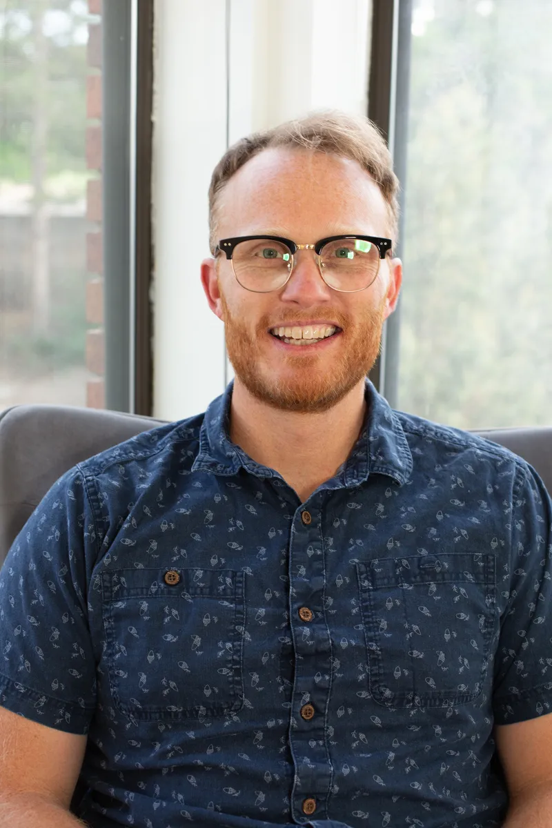Eric Tulga, a counselor with a red beard and glasses, smiling in a sunlit room